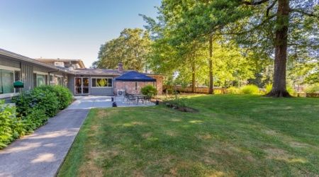 A spacious backyard with a lush lawn, patio area, and surrounding trees, perfect for outdoor relaxation.