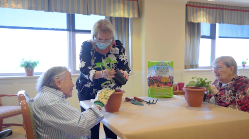 A joyful gardening session where an elderly person receives assistance in potting plants.