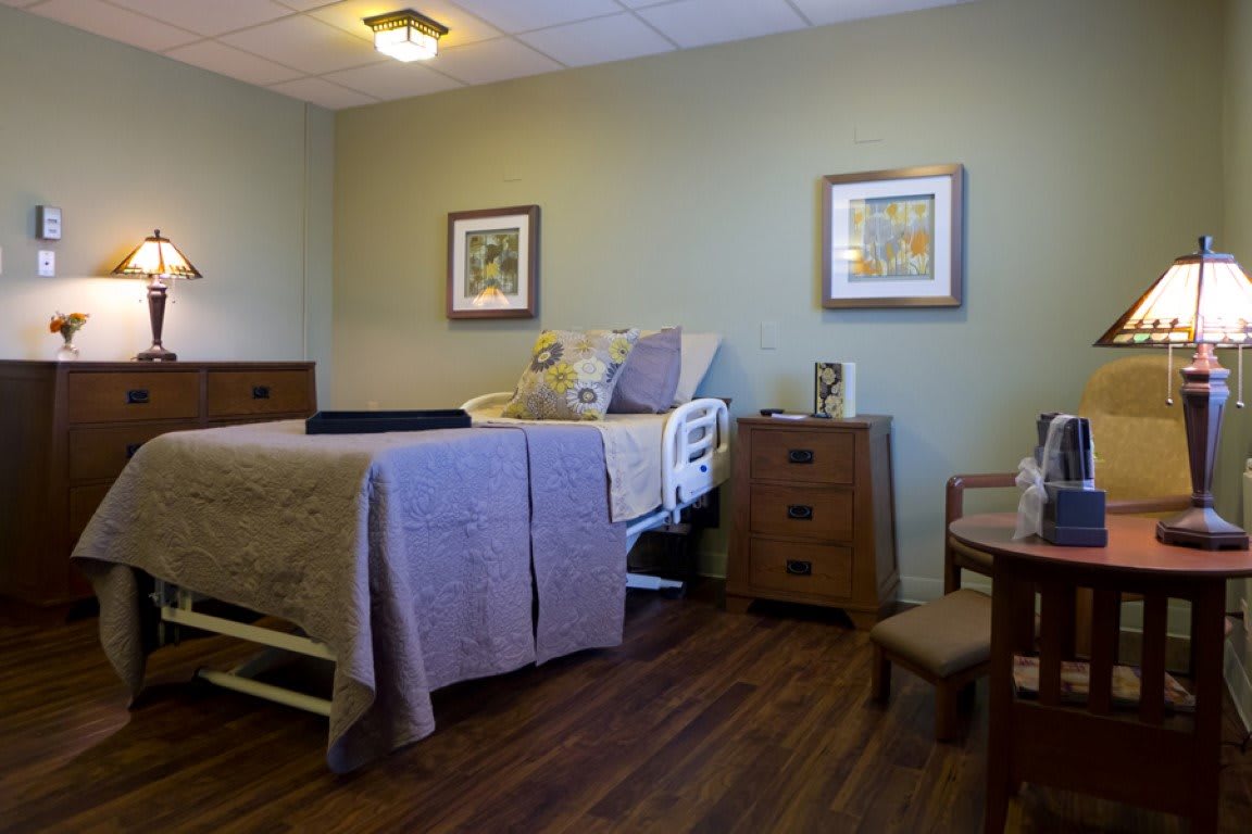 A cozy bedroom with a hospital bed, decorated with paintings and wooden furniture.