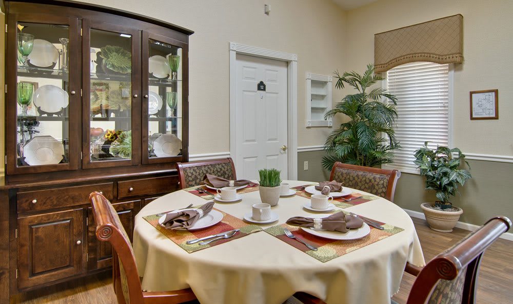 A cozy dining room with a round table set for four, featuring a china cabinet and a decorative plant.