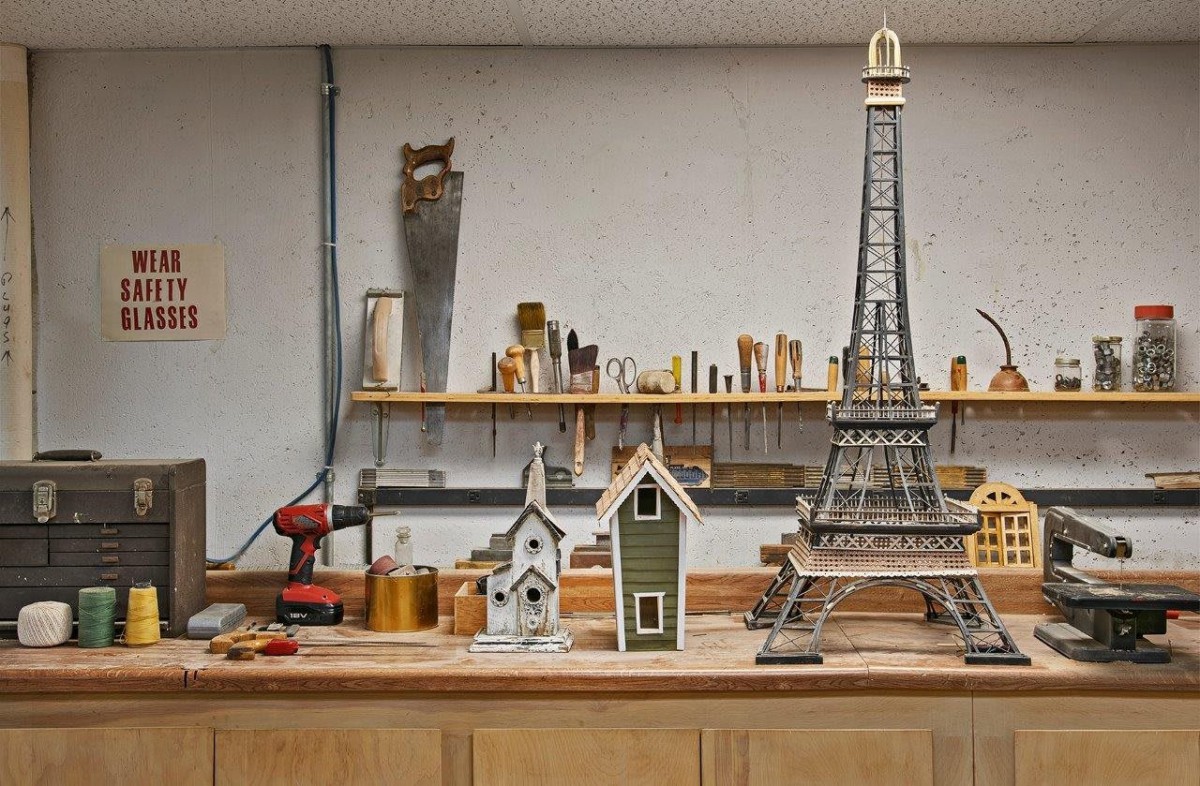 A workshop table displaying miniature models, including an Eiffel Tower replica and birdhouses, surrounded by various tools.