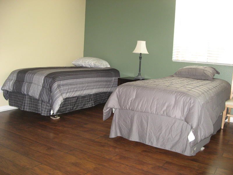 A simple bedroom with two neatly made beds and a lamp on a wooden floor.
