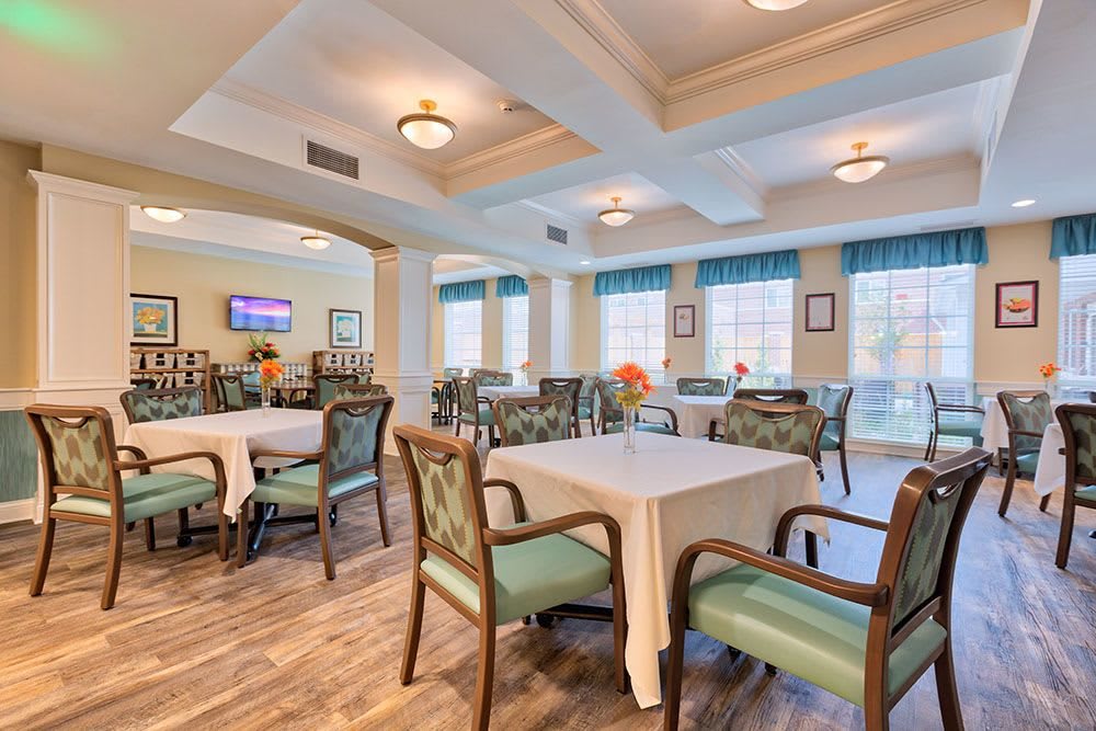 A well-lit dining room with neatly arranged tables and chairs, featuring large windows and elegant lighting fixtures.