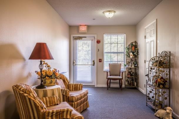 A cozy living room area with striped armchairs, a lamp, and a window near the entrance door.