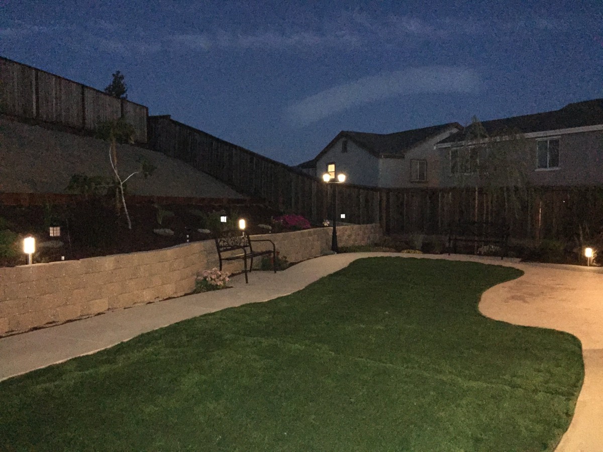 A well-lit backyard at night with artificial grass and a surrounding fence.