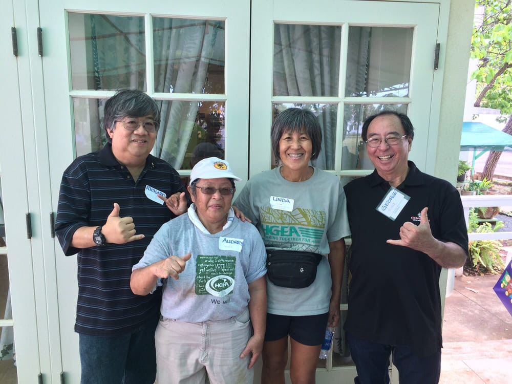 A group of four people posing together indoors, smiling and dressed casually.