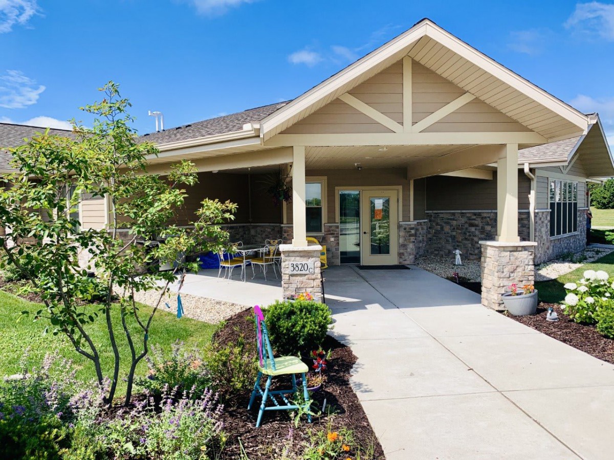 A charming residential house with a covered porch and landscaped garden, set under a clear blue sky.