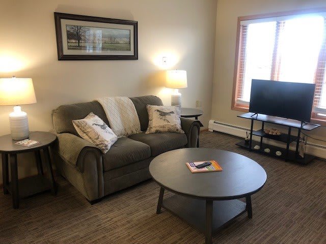 A cozy living room with a sofa, coffee table, lamp, and television by the window.