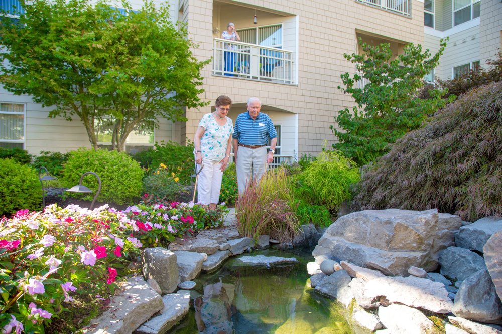 A senior couple enjoying the view of a garden with a pond outside their residential building.