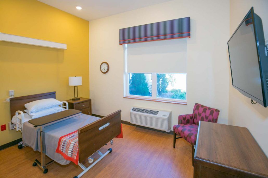 A clean and well-organized hospital room with a bed, furniture, and a window.