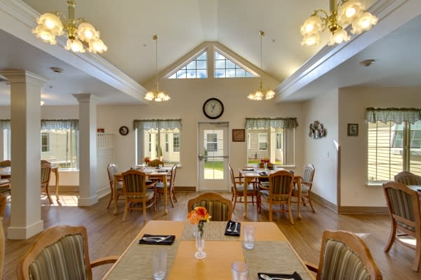 A bright dining room with multiple tables and chairs, featuring large windows and elegant lighting fixtures.