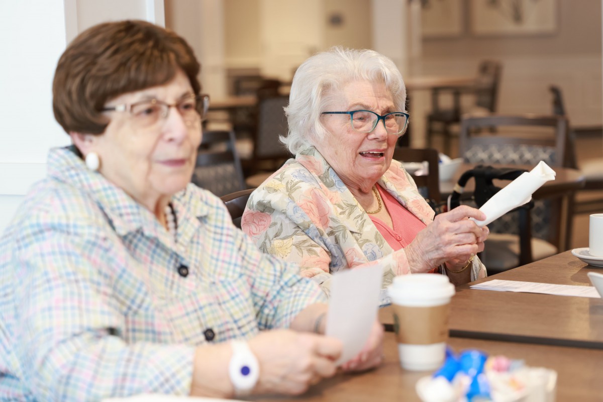 Two senior women enjoying an activity together indoors, with coffee on the table.