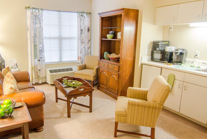 A cozy living room with comfortable chairs, a wooden table, and a shelving unit near a large window.
