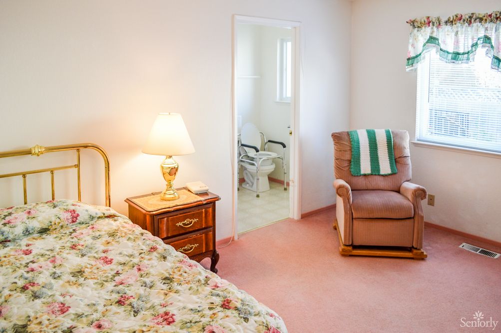 A cozy bedroom with floral bedding, a nightstand with a lamp, and an armchair.