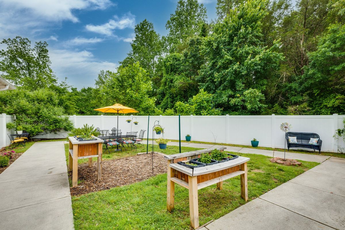 A backyard garden with raised beds, patio furniture, and a white privacy fence.