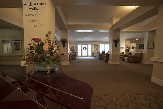 A spacious lobby with a piano and floral arrangement, leading to a well-lit hallway.