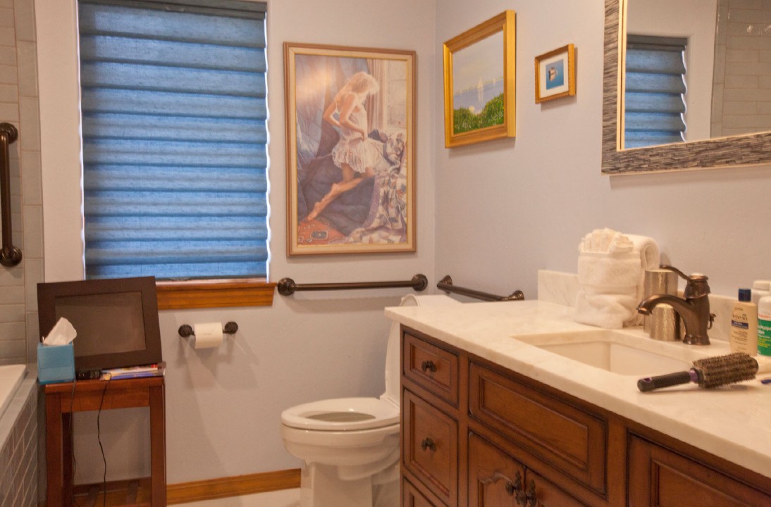 A cozy bathroom with artwork on the walls, featuring a toilet, sink, and mirror.