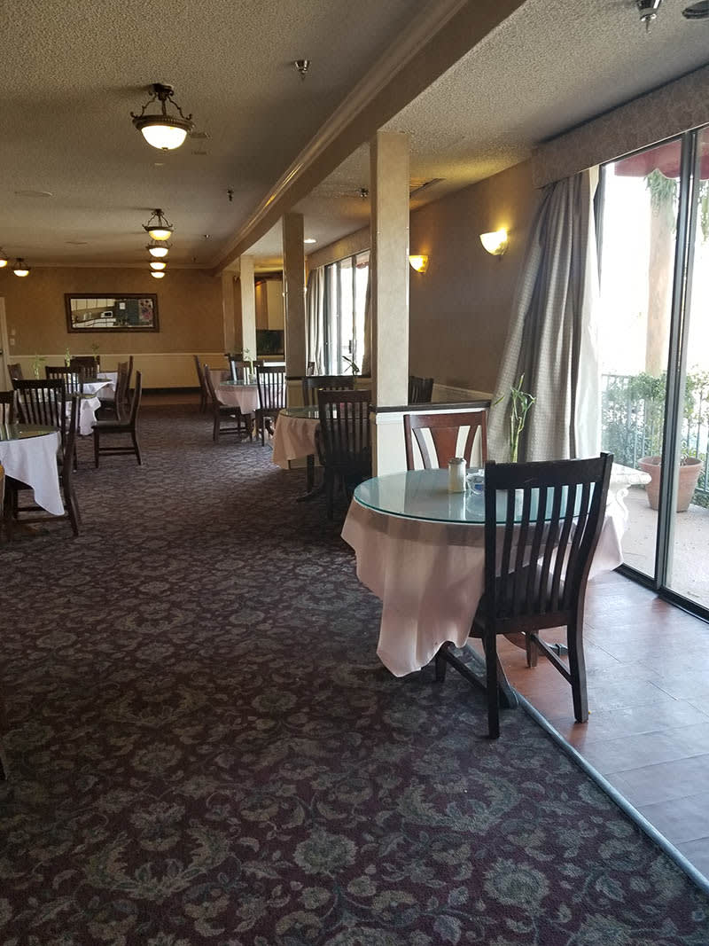 A quiet restaurant dining area with tables and chairs near large windows.