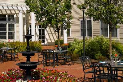 A serene outdoor patio with tables, chairs, and a fountain surrounded by lush greenery and flowers.
