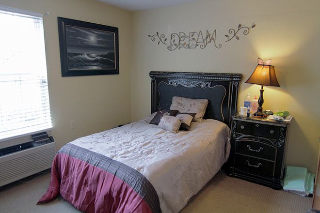 A cozy bedroom with a neatly made bed, wall artwork, and a bedside lamp.