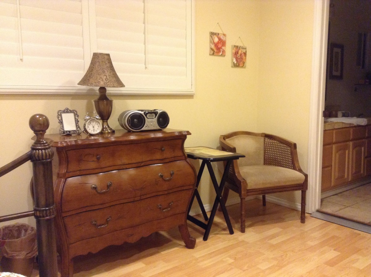 A cozy corner featuring a vintage wooden dresser adorned with decorative items, a lamp, and a comfortable chair.