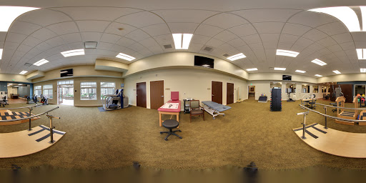 A panoramic view of a medical or hospital room, featuring office furniture and a patient bed.