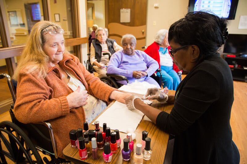A group of elderly women in a care home receiving manicures as part of a group activity.