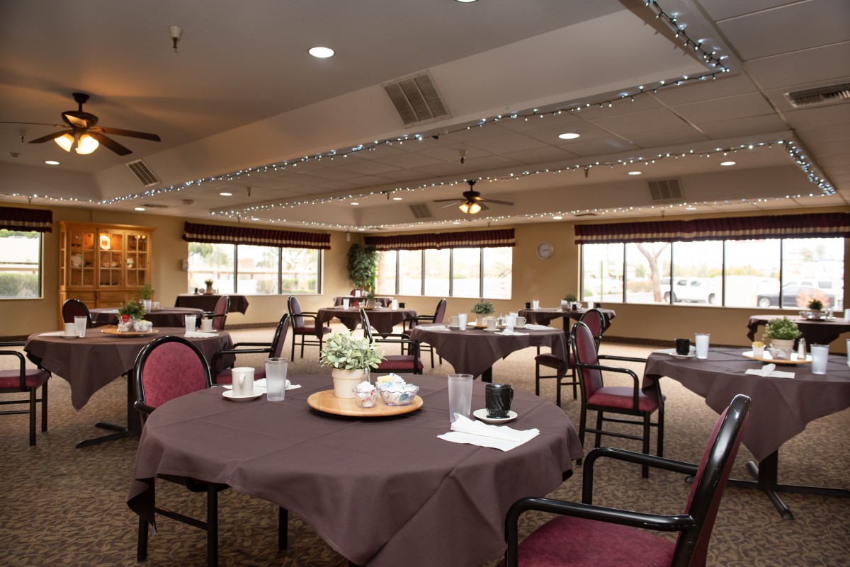 A well-decorated dining room with neatly arranged tables and chairs, featuring elegant lighting and window views.