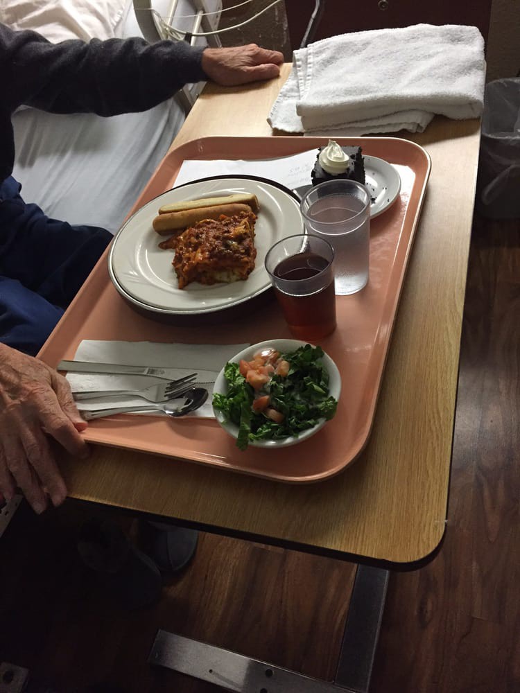 A hospital meal tray featuring lasagna, salad, and a cup of water.