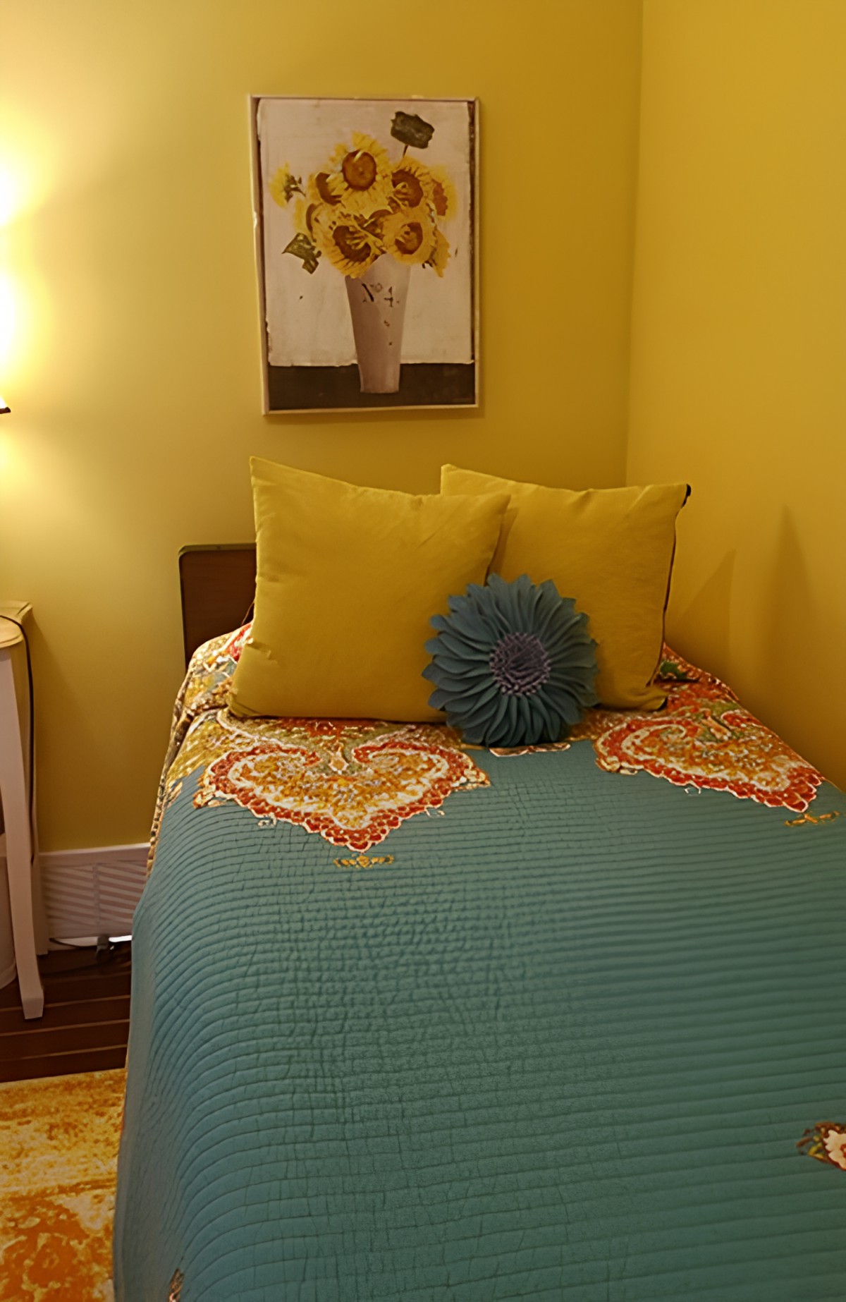 A cozy bedroom with a single bed featuring colorful bedding and decorative pillows against yellow walls.
