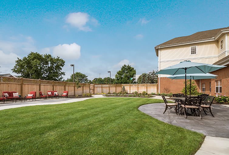 A spacious backyard with a well-maintained lawn, patio furniture under an umbrella, and a wooden fence.