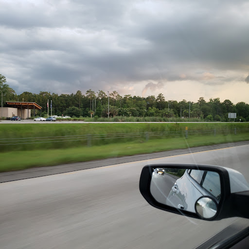 A view from a car window capturing the road and distant greenery under a cloudy sky.