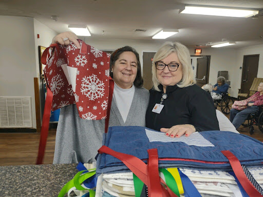 Two smiling women proudly displaying handmade items at a community charity event.