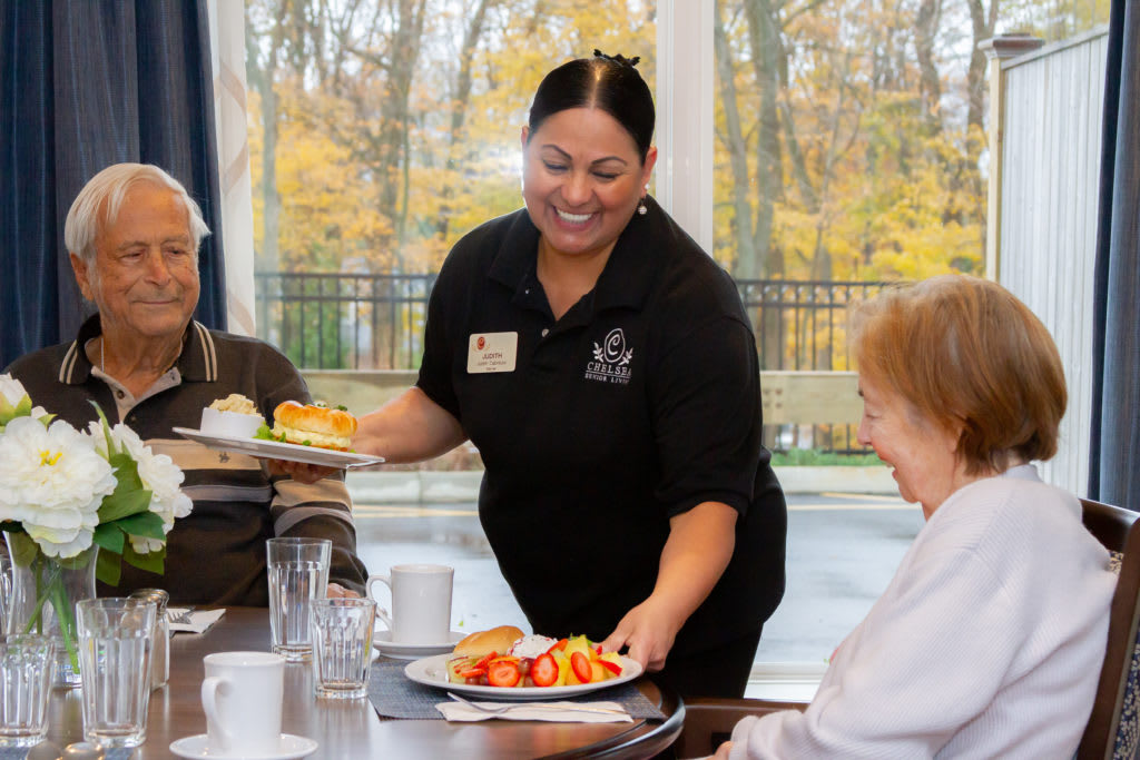 A smiling server delivering meals to elderly diners at a restaurant.