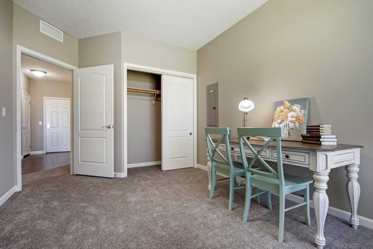 A cozy bedroom with a desk, two chairs, and an open closet.