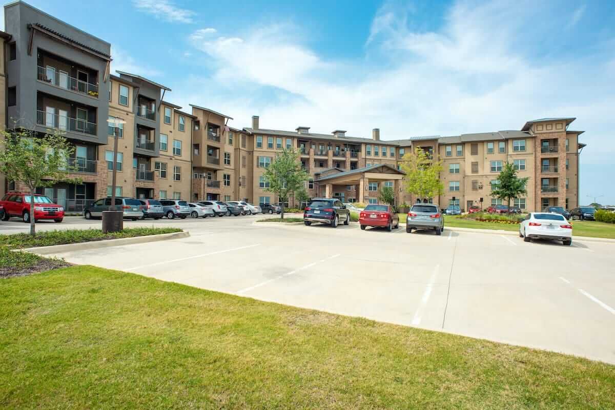 A spacious parking lot in front of a modern apartment complex on a clear day.