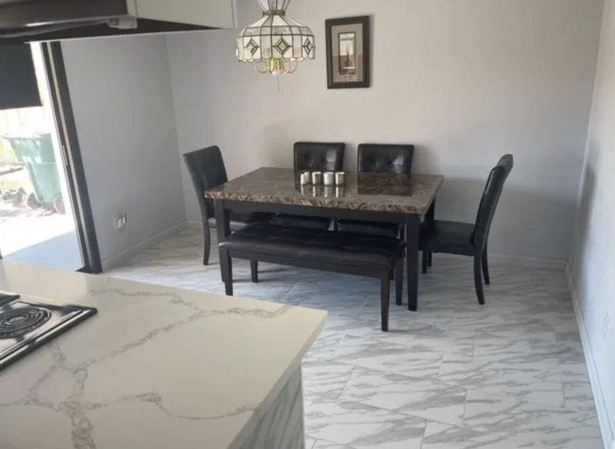A modern dining room with a marble floor, featuring a dark wooden dining table, chairs, and bench seating under a stylish chandelier.