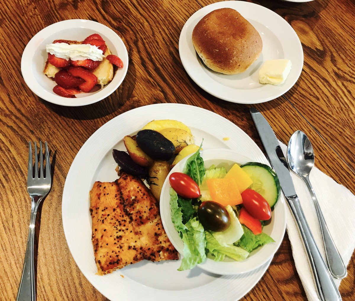 A breakfast spread including toast, salad with fresh vegetables, fruit bowl, and bread roll.