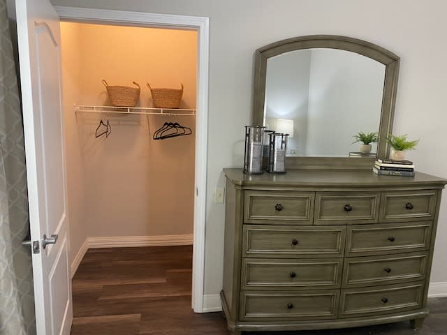 A bedroom setup featuring a dresser with a mirror and an adjacent empty closet.