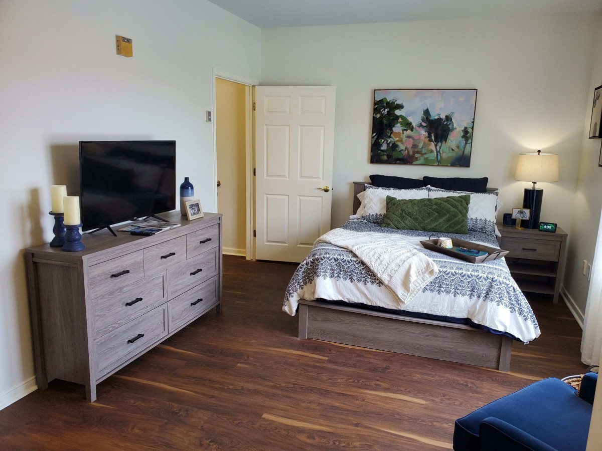 A cozy bedroom with a neatly made bed, dresser with a TV on top, and stylish decor.
