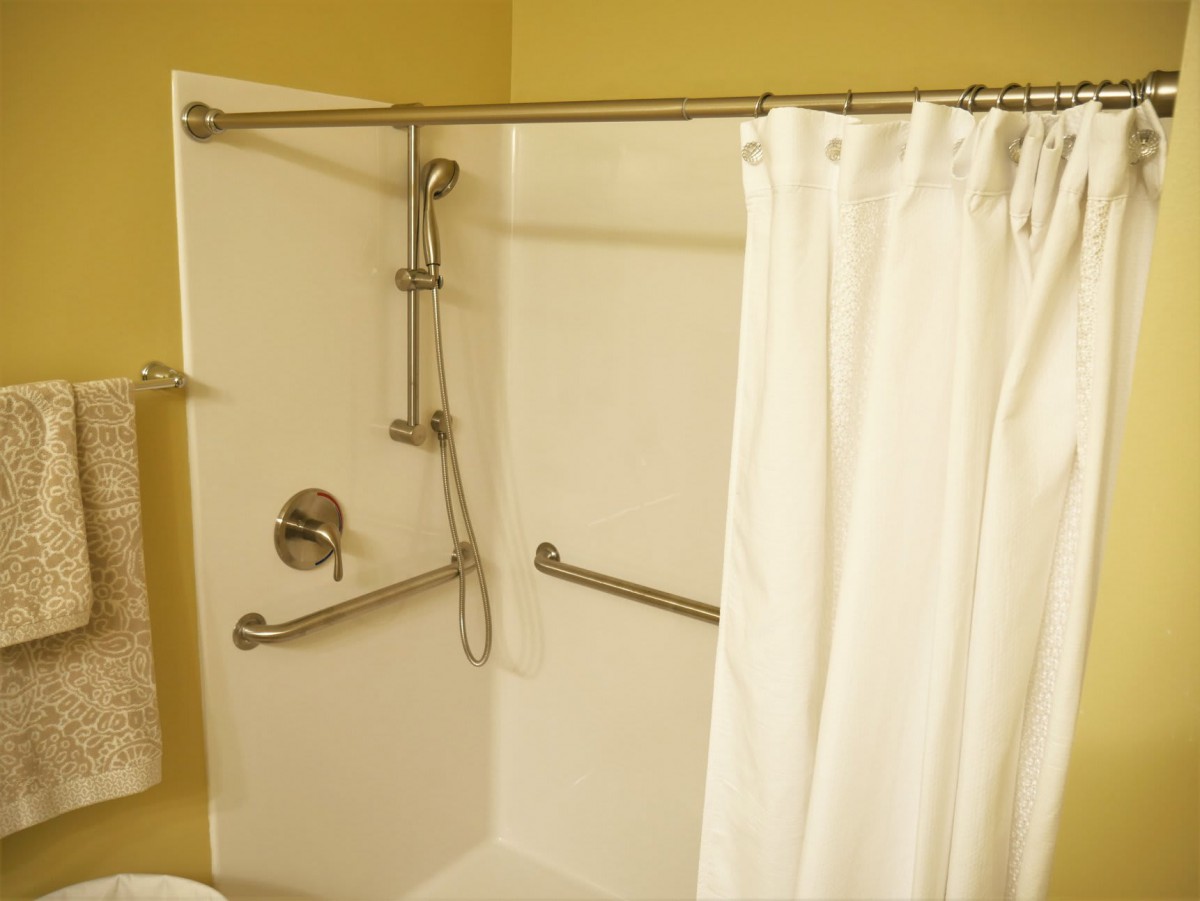 A bathroom with an accessible shower featuring grab bars and a handheld showerhead, enclosed by a white curtain.