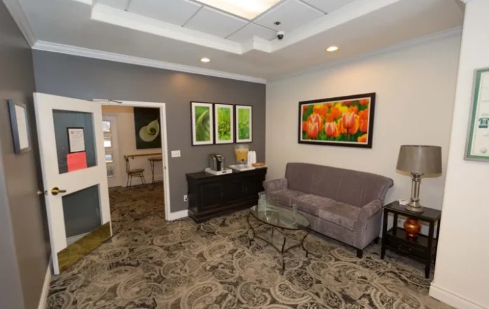 A cozy waiting room with a sofa, artwork on the walls, and a patterned carpet.