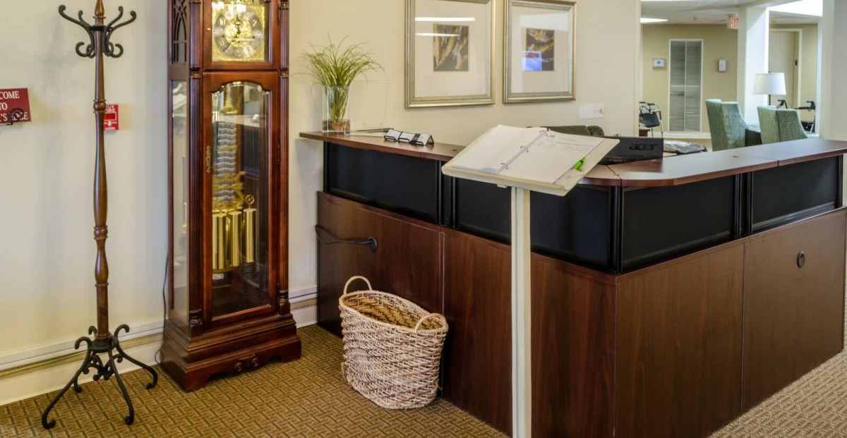 A reception area featuring a desk, grandfather clock, decorative plant, and wall art.