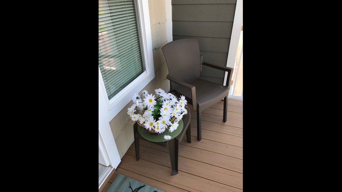 A cozy patio setup with a chair and a small table adorned with a daisy flower arrangement.