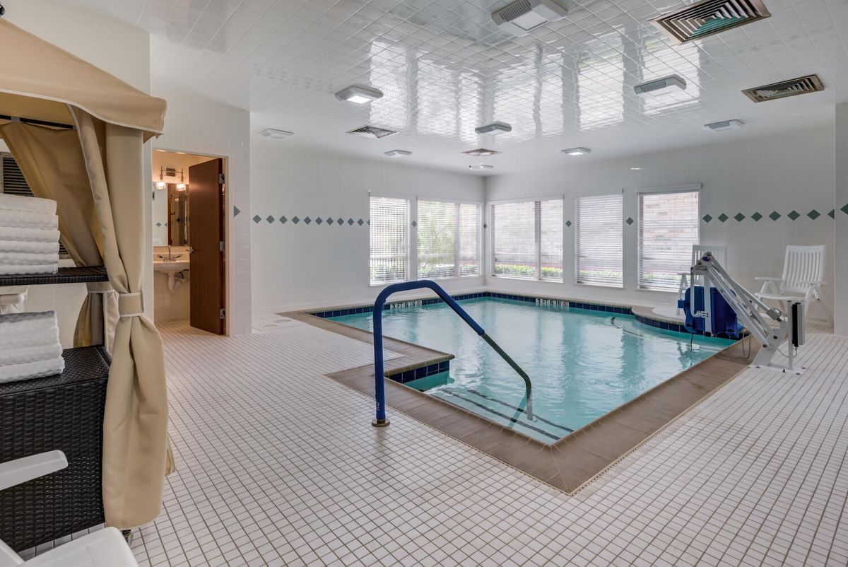 An indoor swimming pool with a tiled floor and handrail, surrounded by large windows.