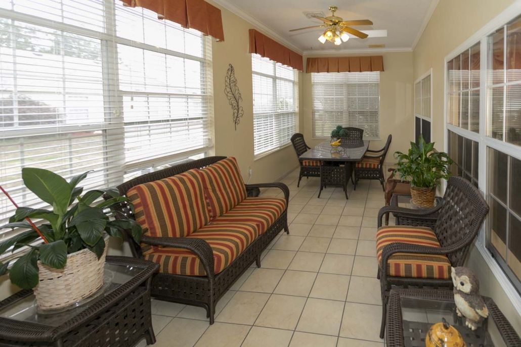 A sunroom featuring wicker furniture with striped cushions, a dining set, and large windows with blinds.