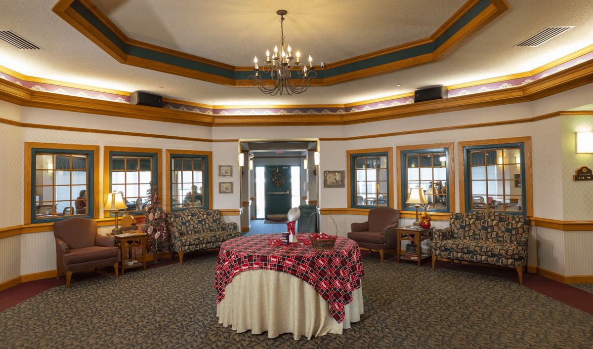 A vintage-style lobby area with a chandelier, surrounded by windows and furnished with comfortable seating.
