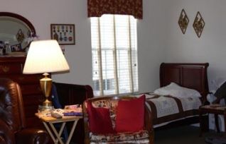 A cozy bedroom with a bed, lamp, and window, featuring decorative elements.