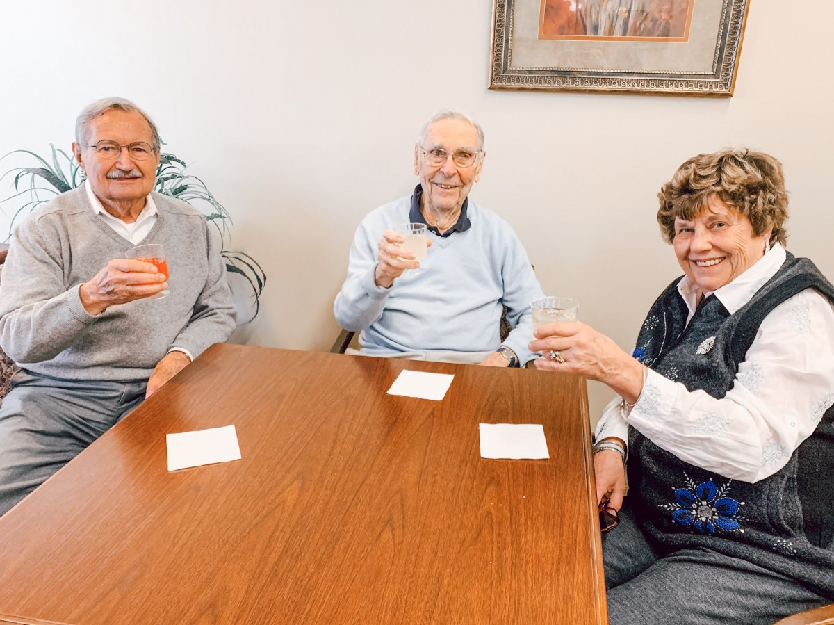 Three seniors sitting at a table, smiling and holding drinks.