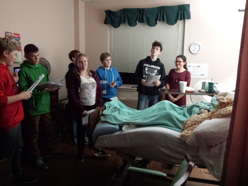 A group of young individuals visiting a patient in a hospital room.
